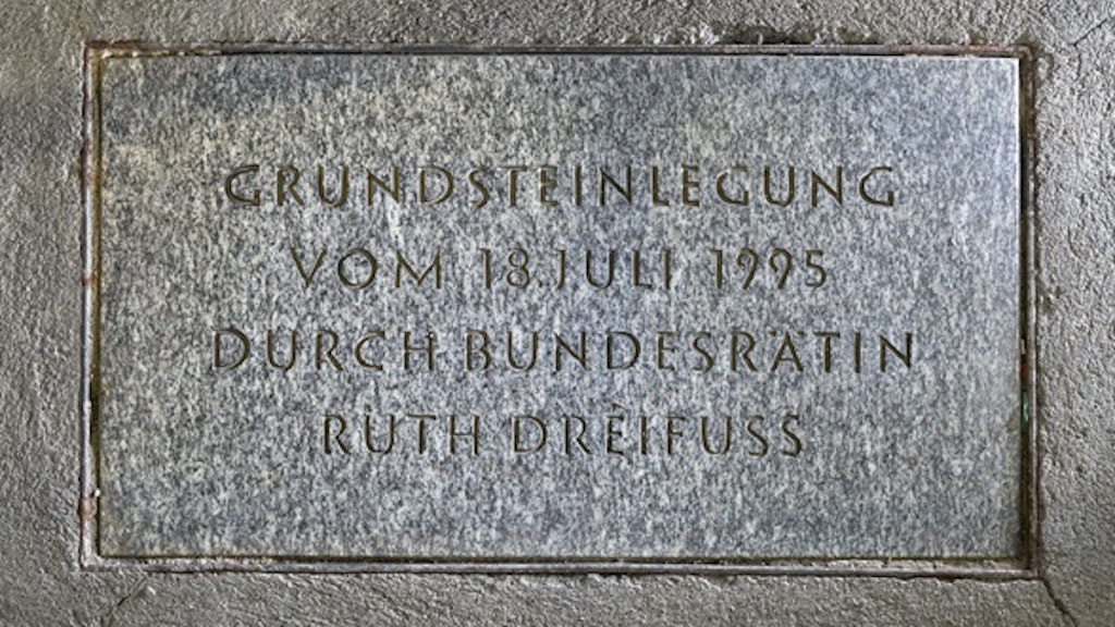 L’iscrizione sulla lastra di pietra grigia venata commemora la posa della prima pietra da parte della consigliera federale Ruth Dreifuss il 18 luglio 1995.