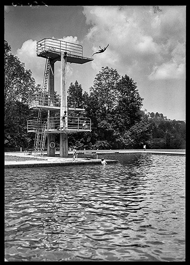 Ein Mann macht im Freibad einen Kopfsprung vom Sprungbrett.