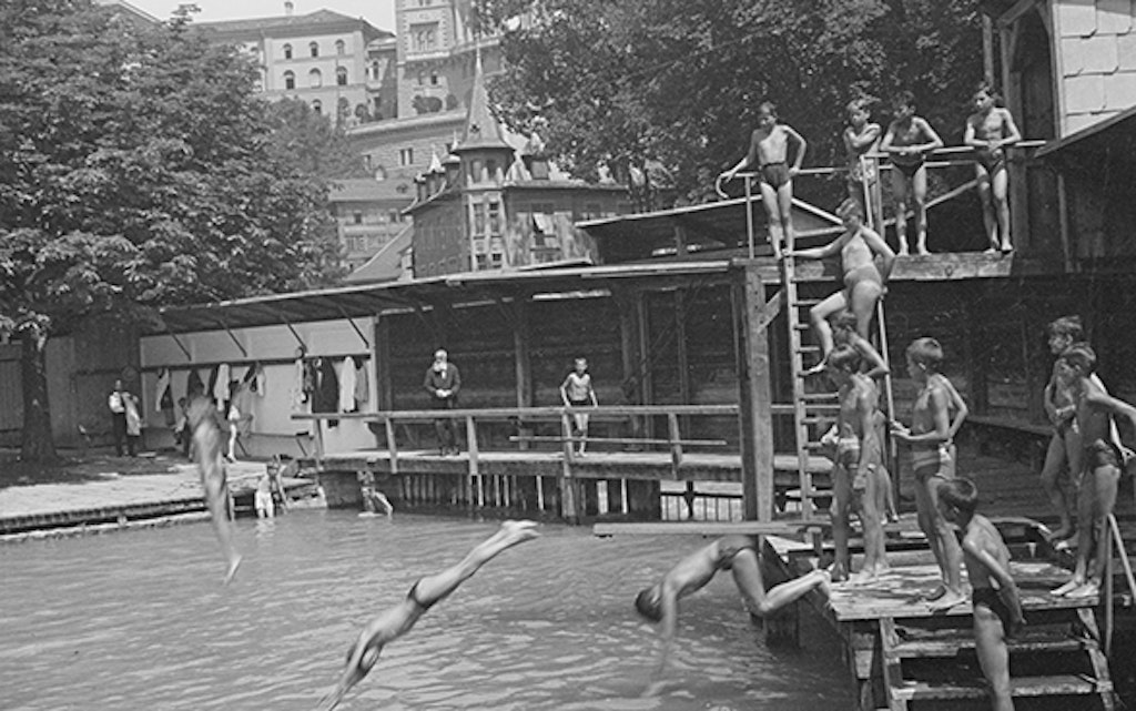 Depiction of three boys at the Marzili open-air bath. They are simultaneously jumping off two diving boards at the edge of the bath in a tributary of the Aare River. Other boys and an older man look on with interest.