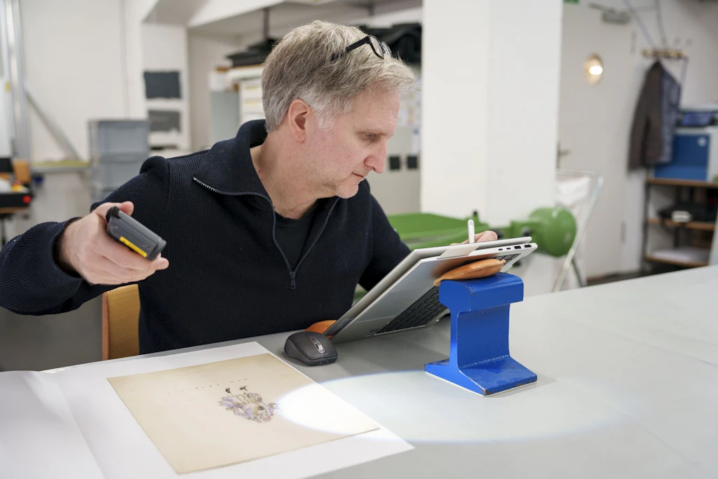 An employee of the National Library checks artwork with a lamp to assess its light sensitivity.