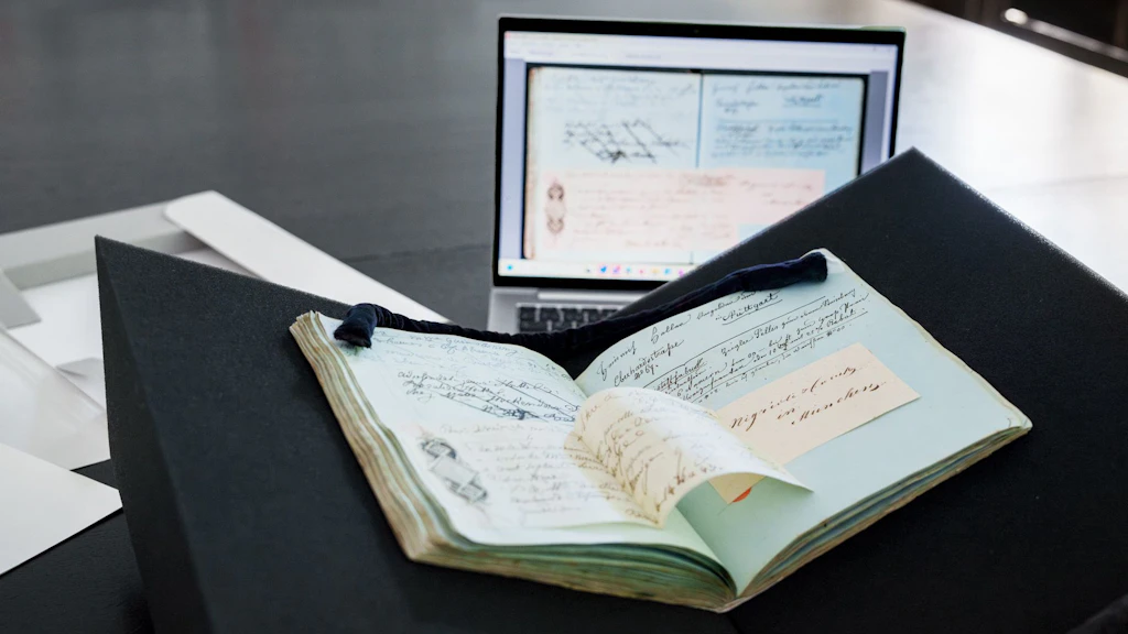 The image shows a screen where work is being done on the digital edition of the original address and order book of Gabriel Mathias Lory, which is lying on the table next to the screen.