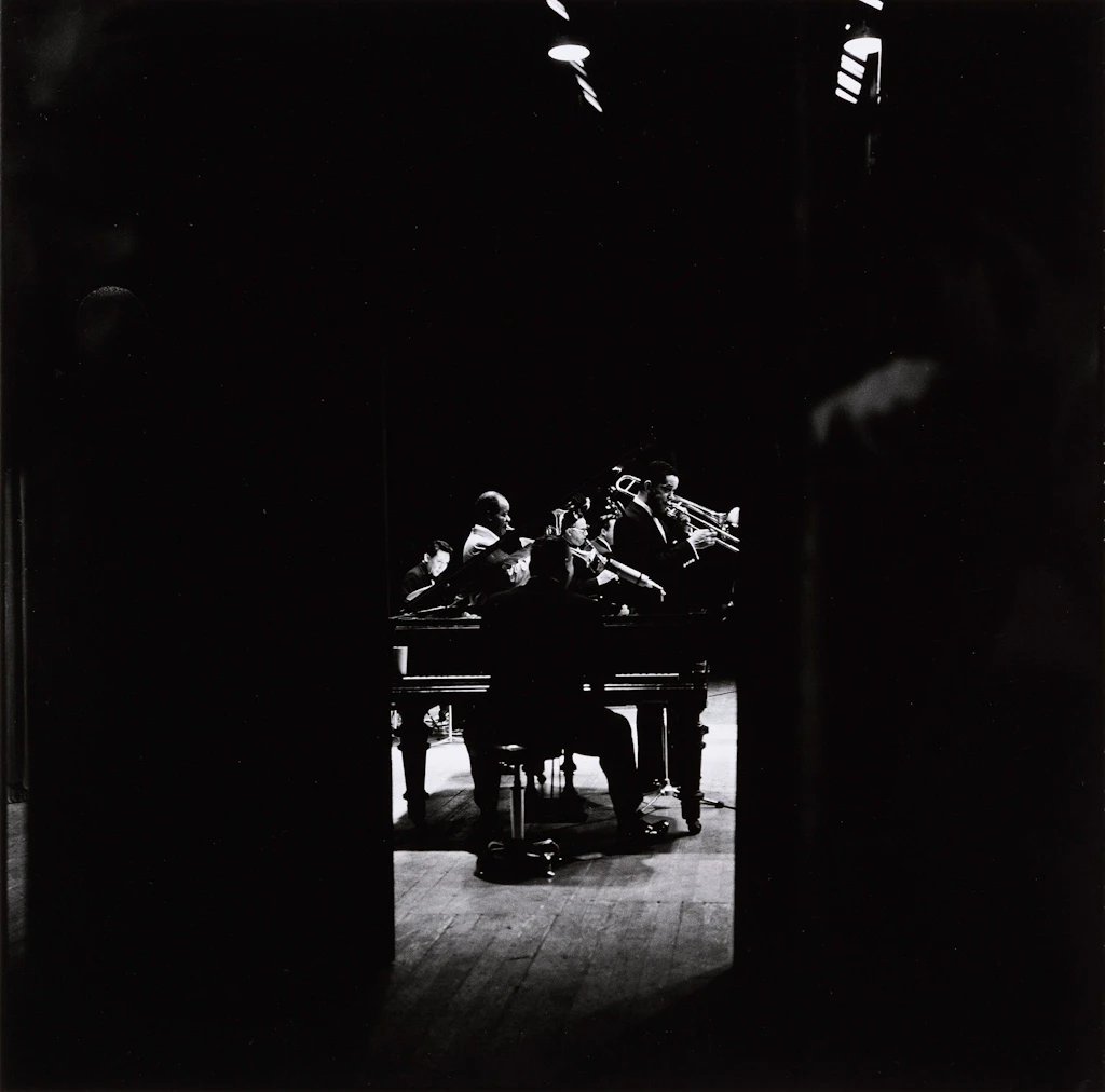 Louis Armstrong and his big band, photographed in profile and through the backstage curtain.