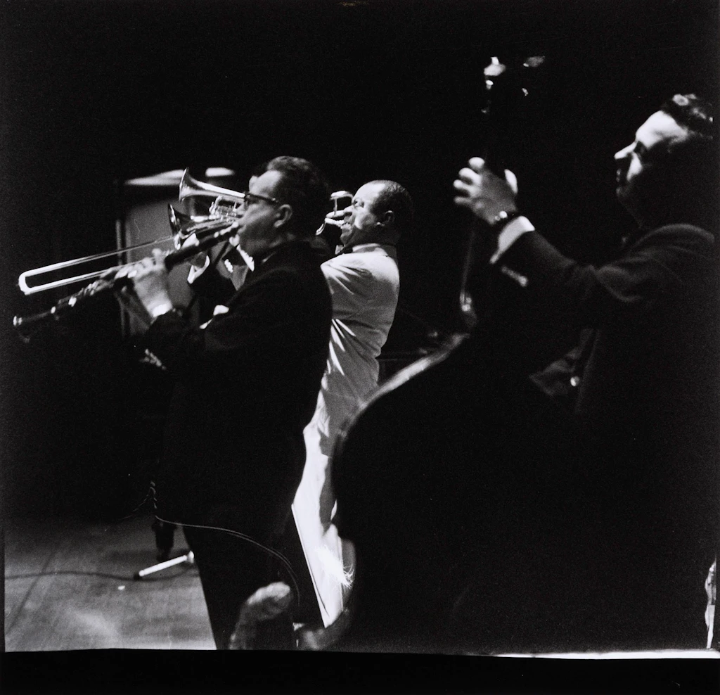 Louis Armstrong, vêtu de blanc, accompagné de deux membres de son groupe vêtus de noir