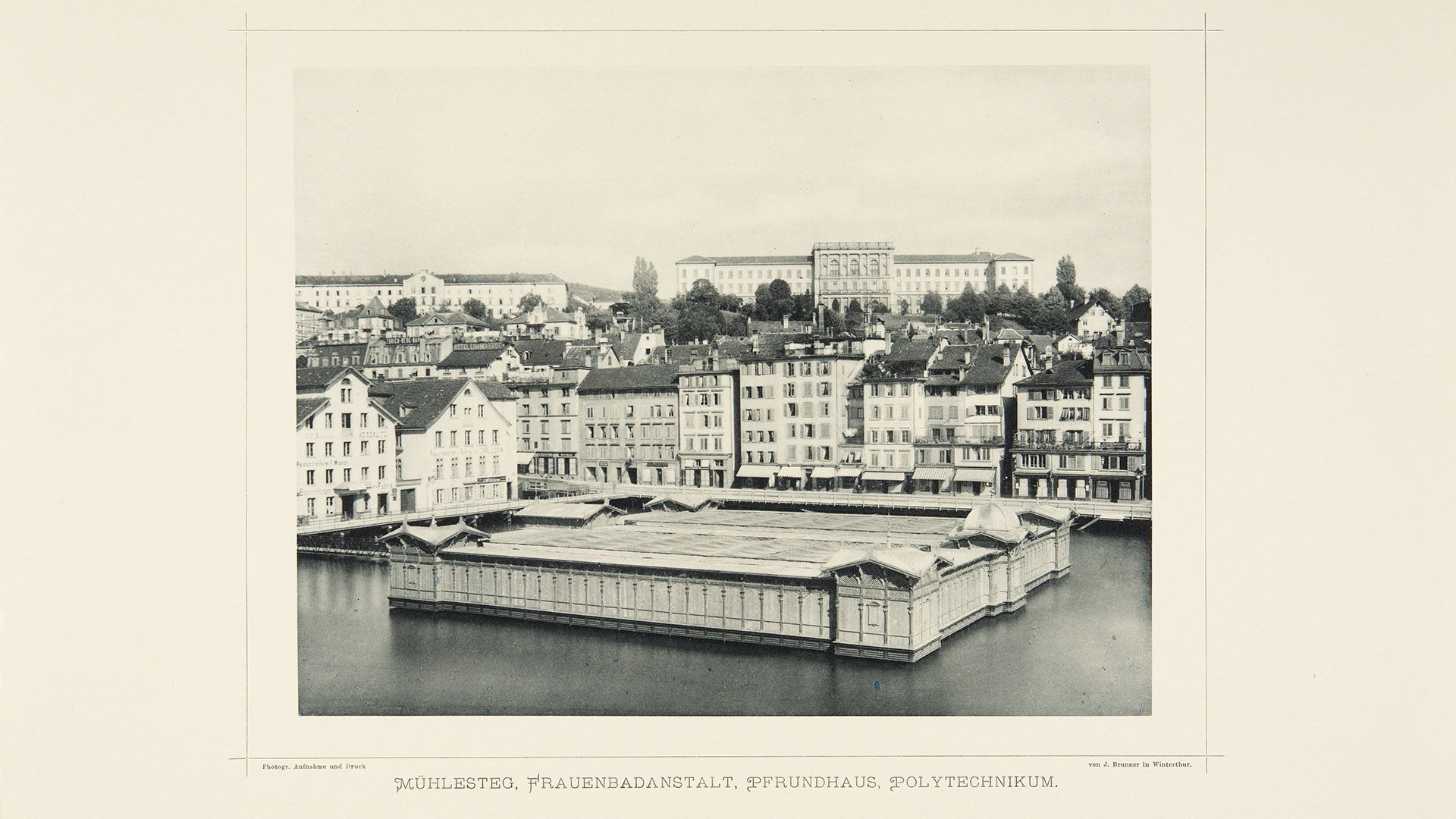 Cette photographie montre le bain pour femmes du Stadthausquai à Zurich, vers 1890. Ce « Kastenbad » est une construction rectangulaire en bois qui flotte sur la Limmat et délimite un espace de baignade protégé. Sur la rive, le bain est entouré d’immeubles d’habitation.