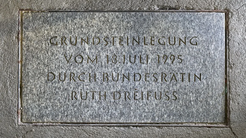 L’inscription sur la dalle en pierre grise mouchetée commémore la pose de la première pierre par la conseillère fédérale Ruth Dreifuss le 18 juillet 1995.