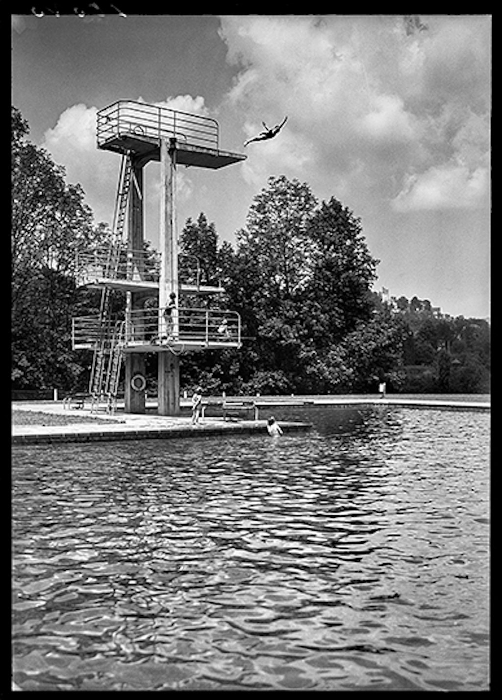 Plongeur effectuant un saut de l’ange depuis le plongeoir d’une piscine en plein air