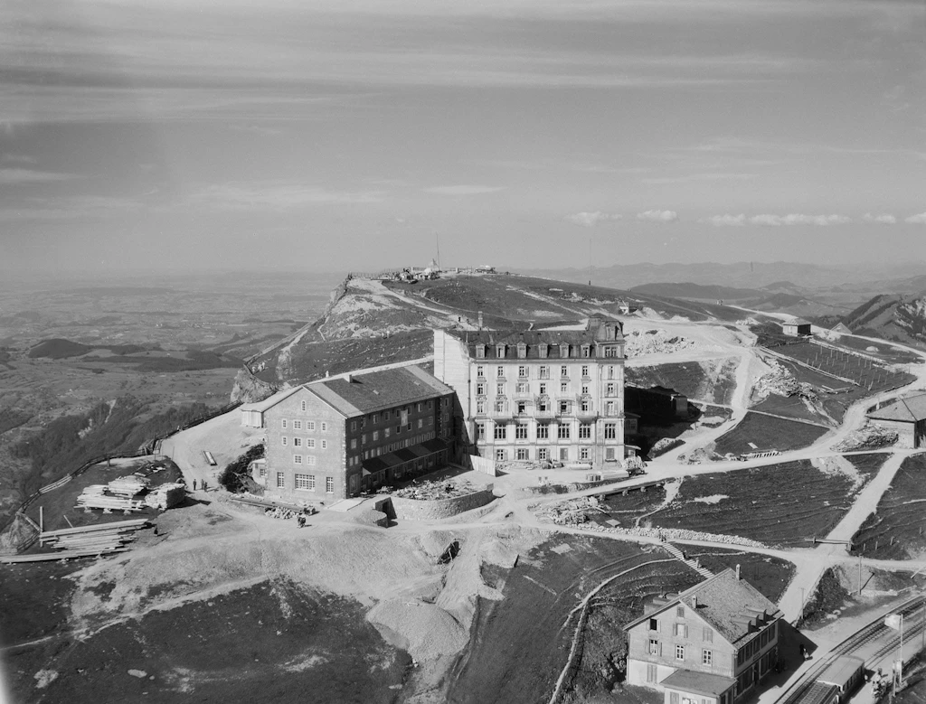 Veduta aerea del Rigi-Kulm con a destra la metà non ancora demolita del Grand Hotel Schreiber e a sinistra il nuovo hotel alpino, circondati da vari percorsi di accesso al cantiere e depositi di materiale (fotografia di Paul Zaugg, Soletta, 1952 circa)