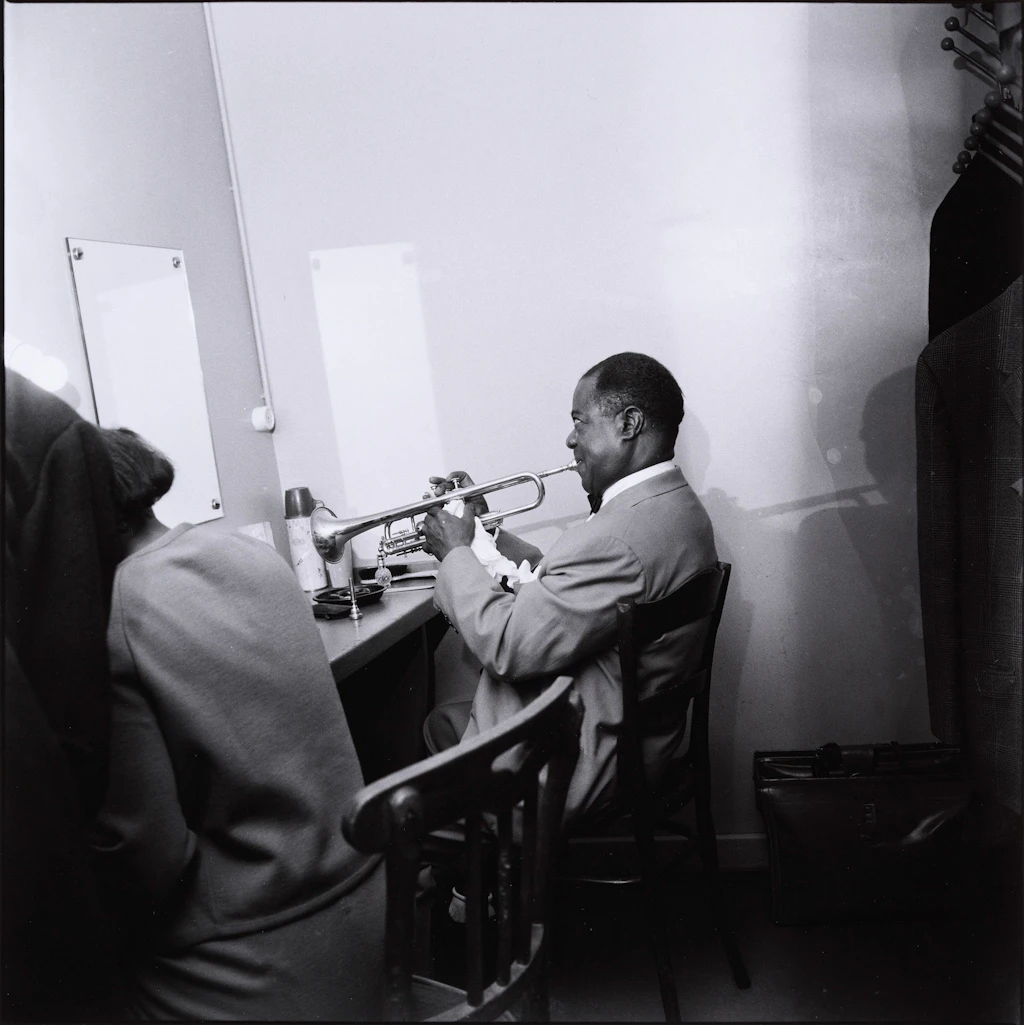 Louis Armstrong seduto nel suo camerino mentre suona la tromba.